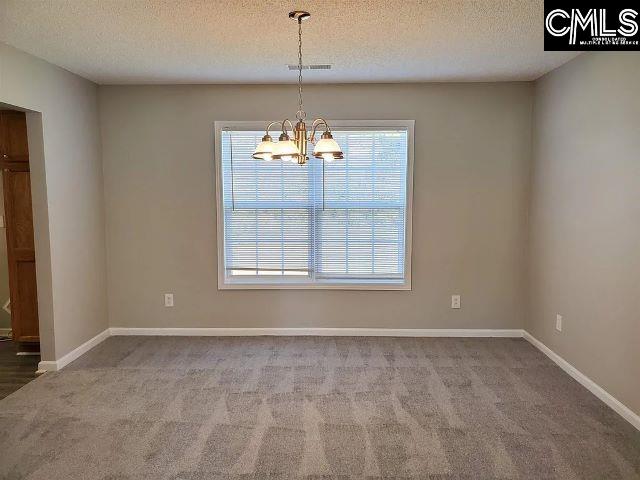 carpeted spare room with a textured ceiling and a chandelier