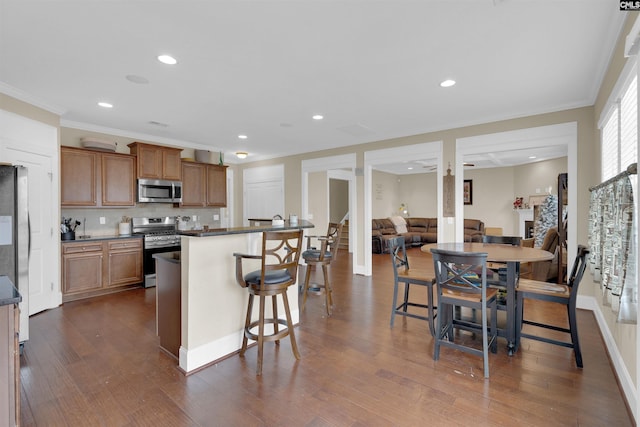 kitchen with dark wood-type flooring, a kitchen bar, decorative backsplash, appliances with stainless steel finishes, and ornamental molding