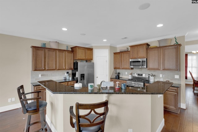 kitchen featuring appliances with stainless steel finishes, crown molding, dark wood-type flooring, and an island with sink