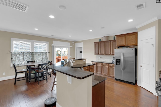 kitchen with a center island with sink, a kitchen breakfast bar, sink, dark hardwood / wood-style floors, and stainless steel fridge