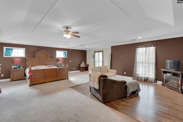 bedroom with ceiling fan, a raised ceiling, light colored carpet, and multiple windows