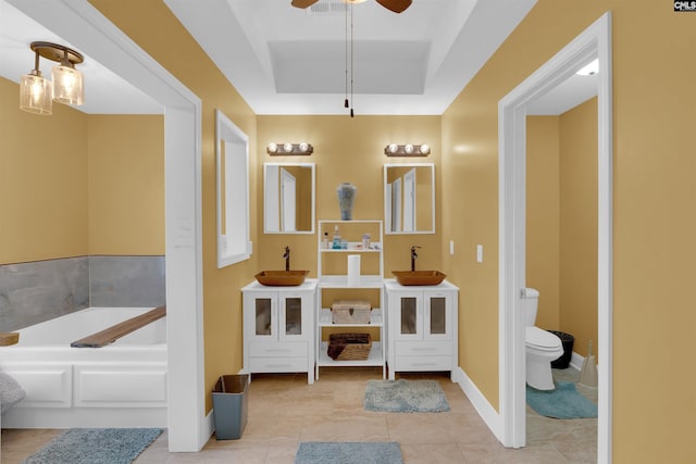 bathroom with tile patterned floors, a tray ceiling, ceiling fan, a bath, and toilet