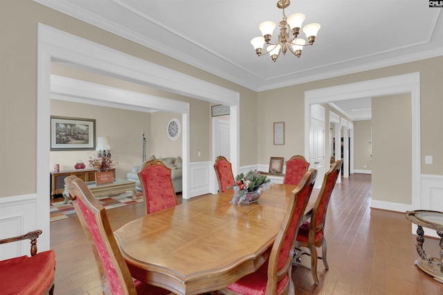 dining space with hardwood / wood-style flooring, crown molding, and an inviting chandelier