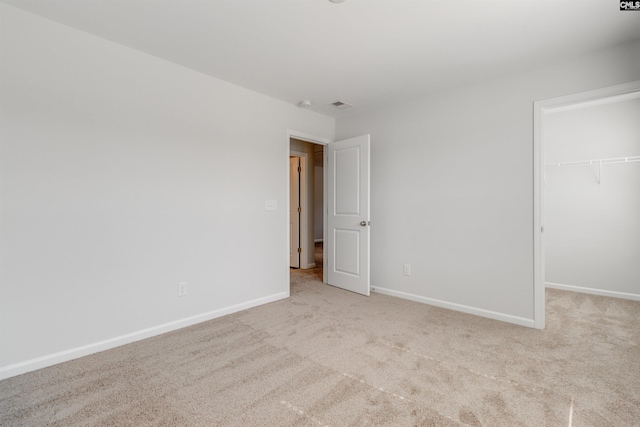 unfurnished bedroom with a walk in closet, a closet, and light colored carpet