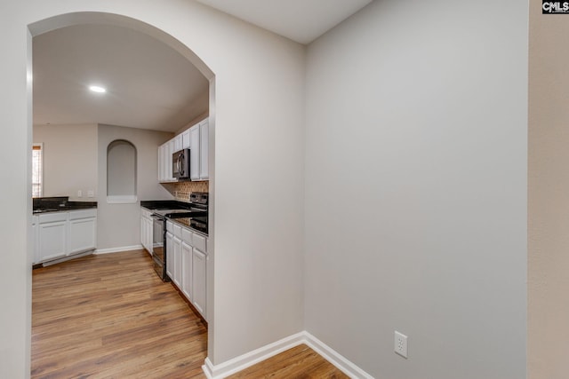 kitchen with black electric range, backsplash, white cabinets, and light hardwood / wood-style flooring