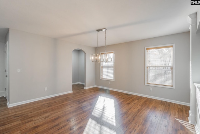 empty room with a chandelier, a wealth of natural light, and dark wood-type flooring