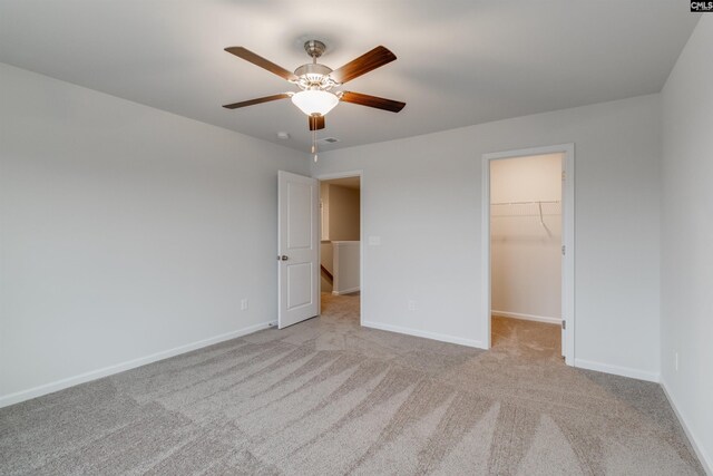 unfurnished bedroom featuring light carpet, a walk in closet, a closet, and ceiling fan