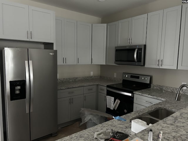 kitchen featuring a sink, appliances with stainless steel finishes, white cabinets, and light stone countertops