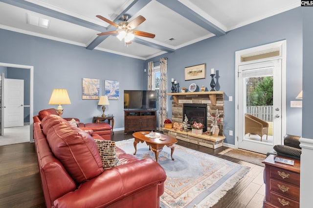 living room with ceiling fan, a stone fireplace, dark hardwood / wood-style flooring, beamed ceiling, and ornamental molding