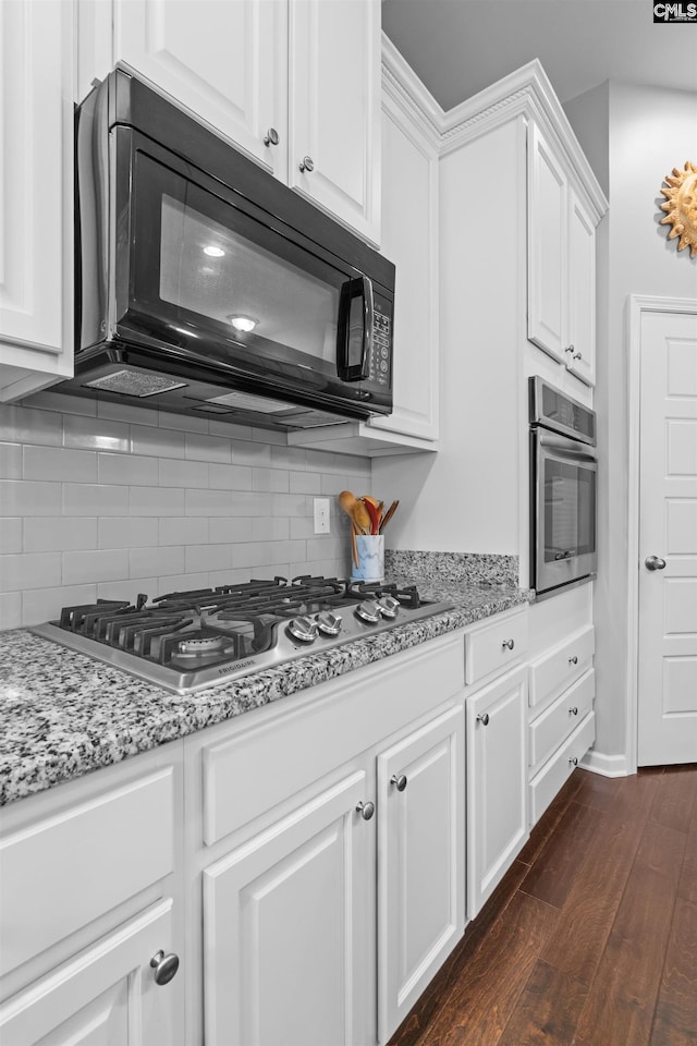 kitchen with decorative backsplash, appliances with stainless steel finishes, light stone countertops, dark wood-type flooring, and white cabinets