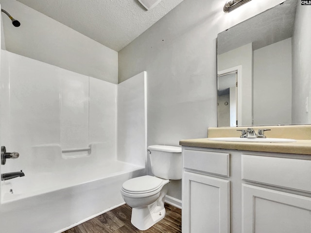 full bathroom with vanity, a textured ceiling, hardwood / wood-style flooring, washtub / shower combination, and toilet