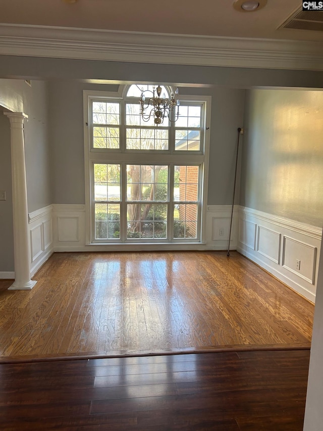 spare room with decorative columns, hardwood / wood-style floors, ornamental molding, and a notable chandelier