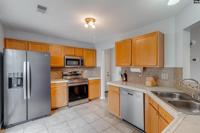 kitchen with a textured ceiling, sink, stainless steel appliances, and tasteful backsplash