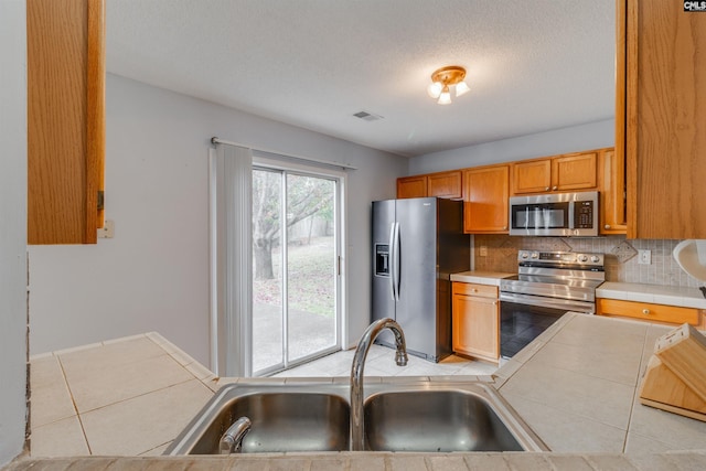 kitchen featuring sink, stainless steel appliances, tile countertops, decorative backsplash, and light tile patterned floors