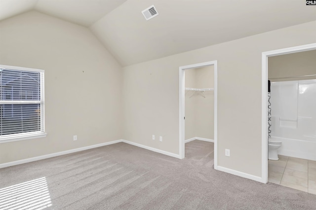 unfurnished bedroom featuring light carpet, a walk in closet, and lofted ceiling