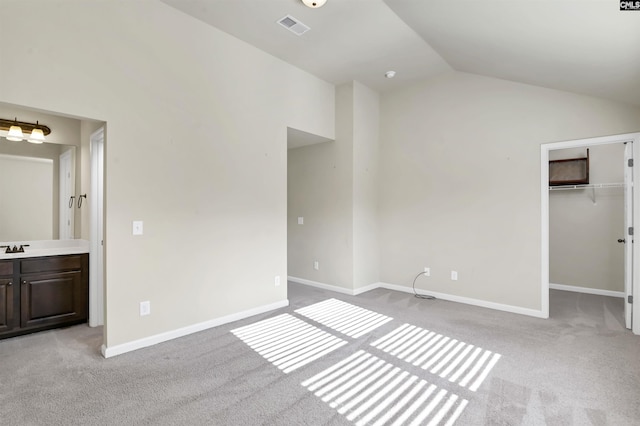 unfurnished bedroom with a walk in closet, light carpet, a closet, and lofted ceiling