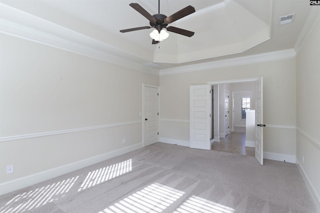 empty room featuring a raised ceiling, crown molding, ceiling fan, and light colored carpet