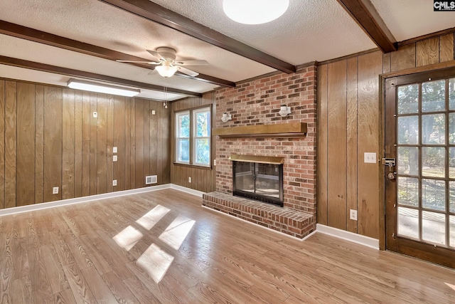 unfurnished living room featuring a brick fireplace, ceiling fan, a textured ceiling, beamed ceiling, and light hardwood / wood-style floors