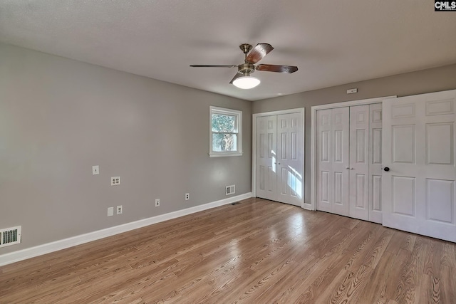 unfurnished bedroom featuring light hardwood / wood-style floors, ceiling fan, and multiple closets