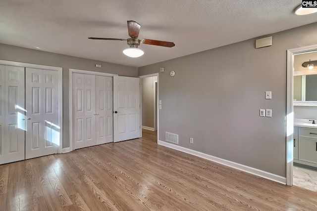 unfurnished bedroom with multiple closets, ceiling fan, ensuite bathroom, a textured ceiling, and light wood-type flooring