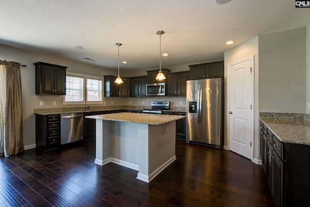 kitchen featuring light stone counters, dark brown cabinetry, stainless steel appliances, dark wood-type flooring, and hanging light fixtures