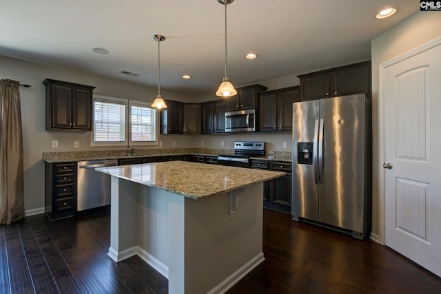 kitchen with a center island, hanging light fixtures, light stone countertops, appliances with stainless steel finishes, and dark hardwood / wood-style flooring