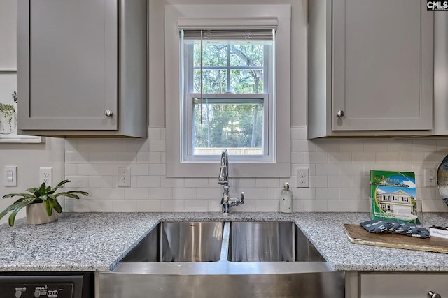 kitchen with plenty of natural light, gray cabinets, light stone counters, and sink