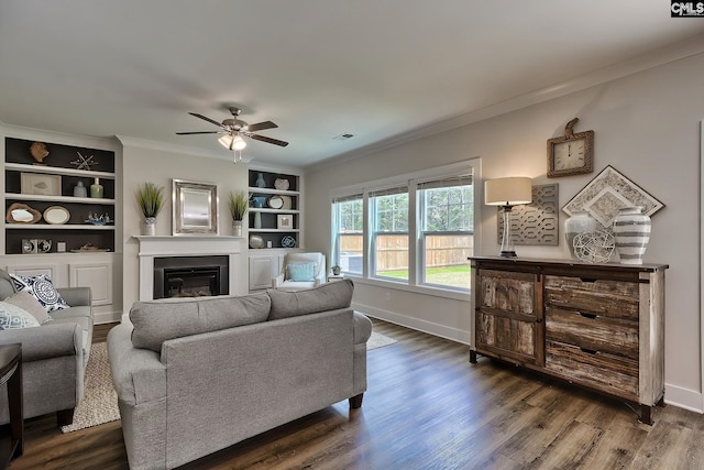 living room with ceiling fan, built in features, ornamental molding, and dark wood-type flooring