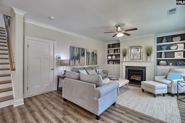 living room featuring crown molding, built in features, ceiling fan, and dark wood-type flooring