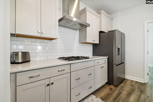 kitchen with wall chimney exhaust hood, dark hardwood / wood-style flooring, decorative backsplash, white cabinets, and appliances with stainless steel finishes