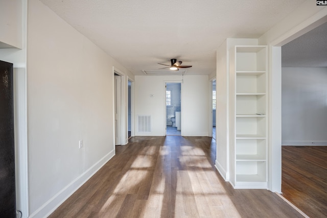 corridor with built in features, wood-type flooring, and a textured ceiling