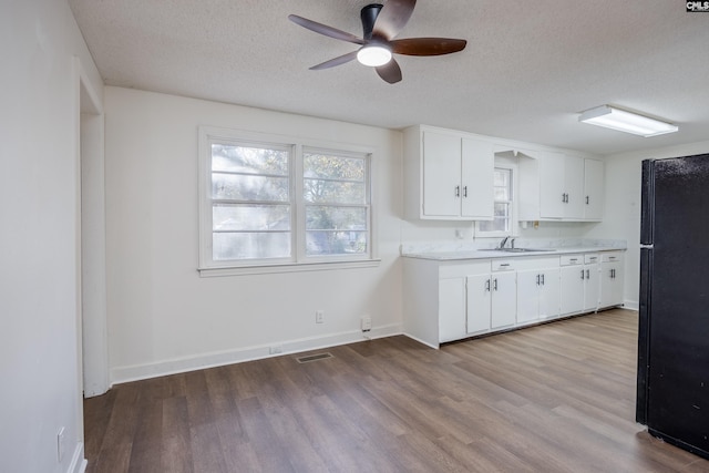 kitchen featuring white cabinetry, sink, black fridge, a textured ceiling, and light wood-type flooring