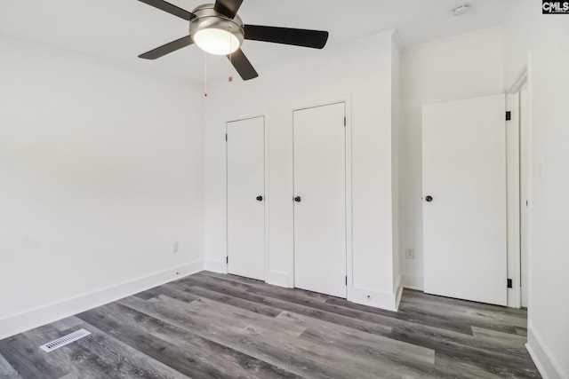 unfurnished bedroom featuring ceiling fan, dark hardwood / wood-style flooring, and two closets