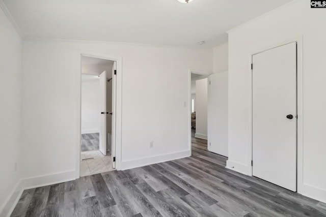 unfurnished bedroom featuring hardwood / wood-style floors, lofted ceiling, ensuite bath, ornamental molding, and a closet