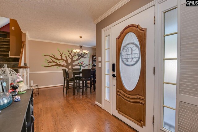 entryway with wood-type flooring, a textured ceiling, an inviting chandelier, and crown molding