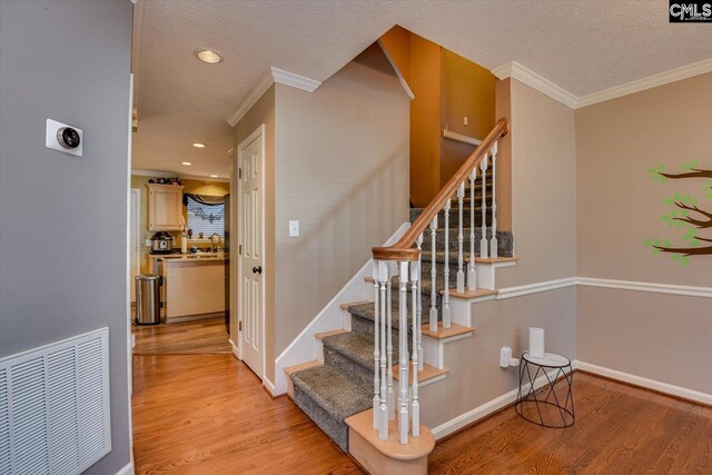 stairway featuring hardwood / wood-style floors, a textured ceiling, crown molding, and sink