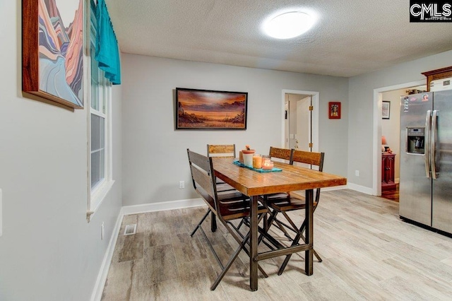 dining space with light wood-type flooring and a textured ceiling