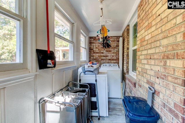 laundry area with washer and dryer, a healthy amount of sunlight, and brick wall