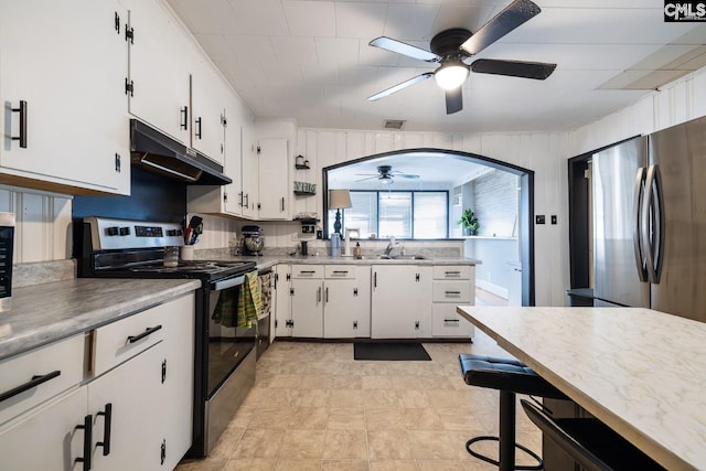 kitchen featuring stainless steel appliances, ceiling fan, sink, white cabinets, and wood walls