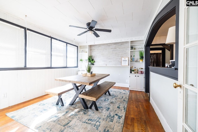 dining room featuring built in shelves, ceiling fan, wood walls, and dark hardwood / wood-style floors