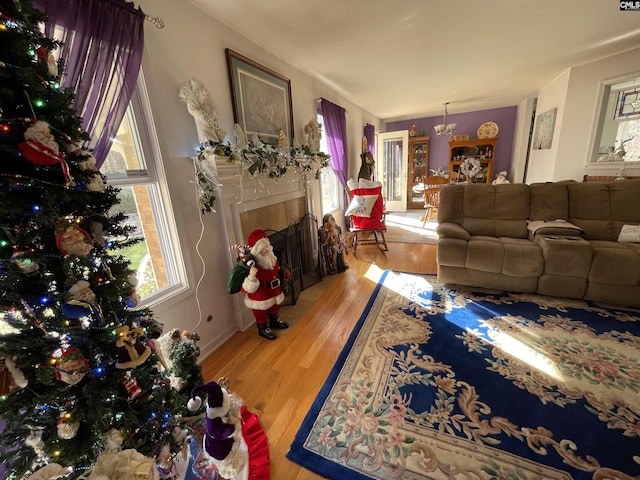 living room with a tiled fireplace, an inviting chandelier, a healthy amount of sunlight, and light hardwood / wood-style floors