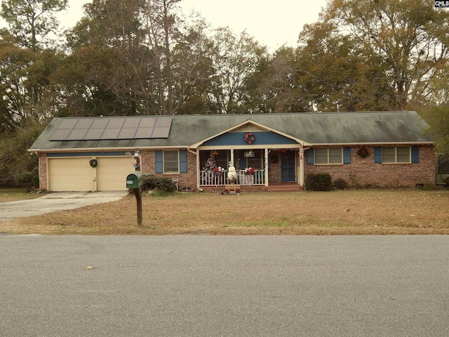 ranch-style home with covered porch, solar panels, a garage, and a front lawn