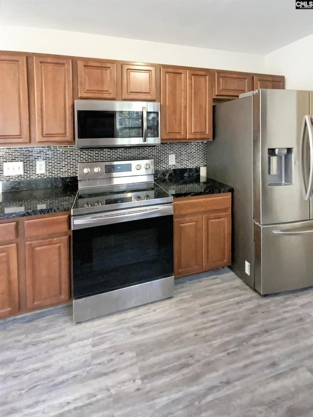 kitchen with backsplash, light hardwood / wood-style floors, dark stone countertops, and stainless steel appliances