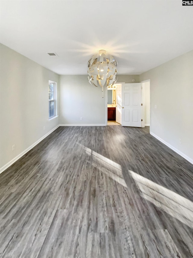 unfurnished room with an inviting chandelier and dark wood-type flooring