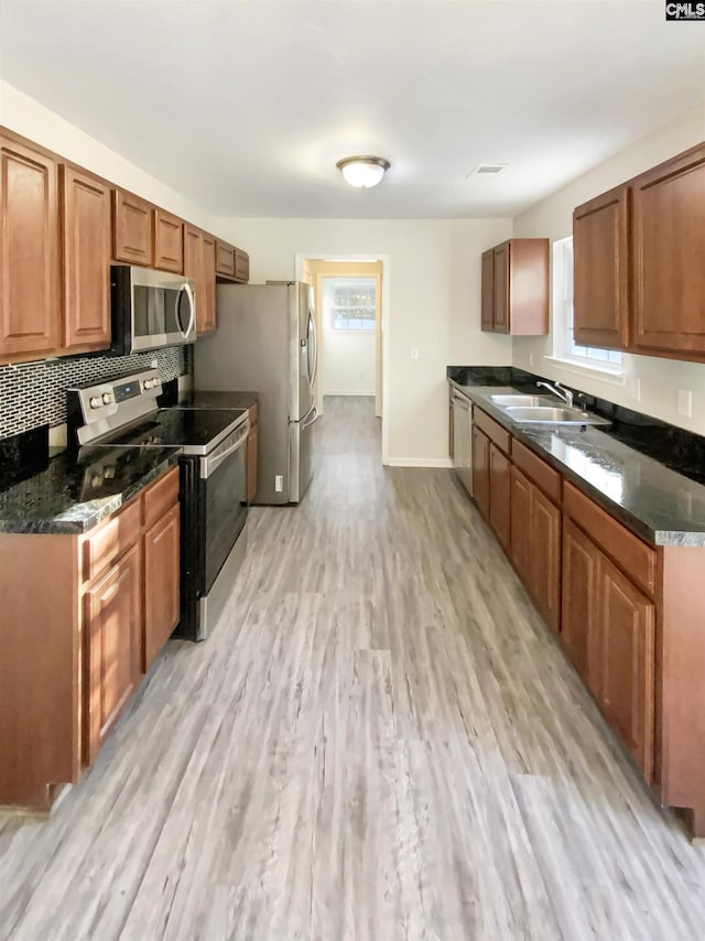 kitchen featuring sink, backsplash, dark stone countertops, appliances with stainless steel finishes, and light wood-type flooring