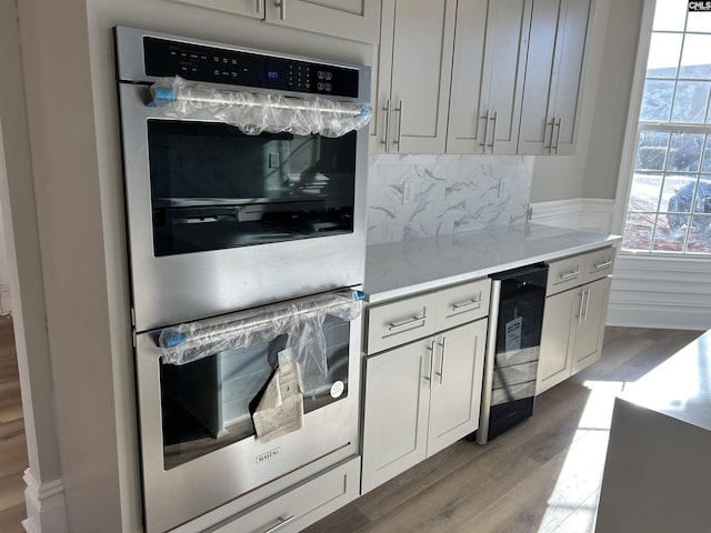 kitchen with stainless steel double oven, tasteful backsplash, wine cooler, hardwood / wood-style floors, and white cabinets