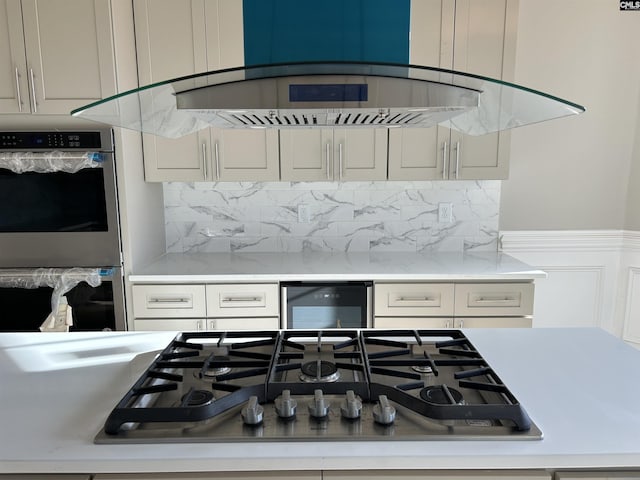 kitchen with ventilation hood, decorative backsplash, stainless steel appliances, and beverage cooler