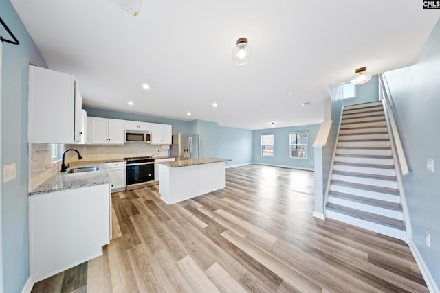 kitchen with sink, light wood-type flooring, appliances with stainless steel finishes, a kitchen island, and white cabinetry