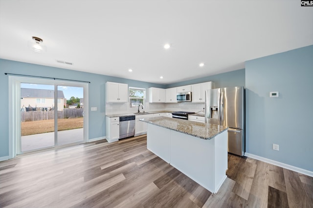 kitchen with light wood-type flooring, stainless steel appliances, sink, white cabinets, and a center island