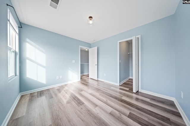 unfurnished bedroom featuring multiple windows, a walk in closet, and light hardwood / wood-style floors